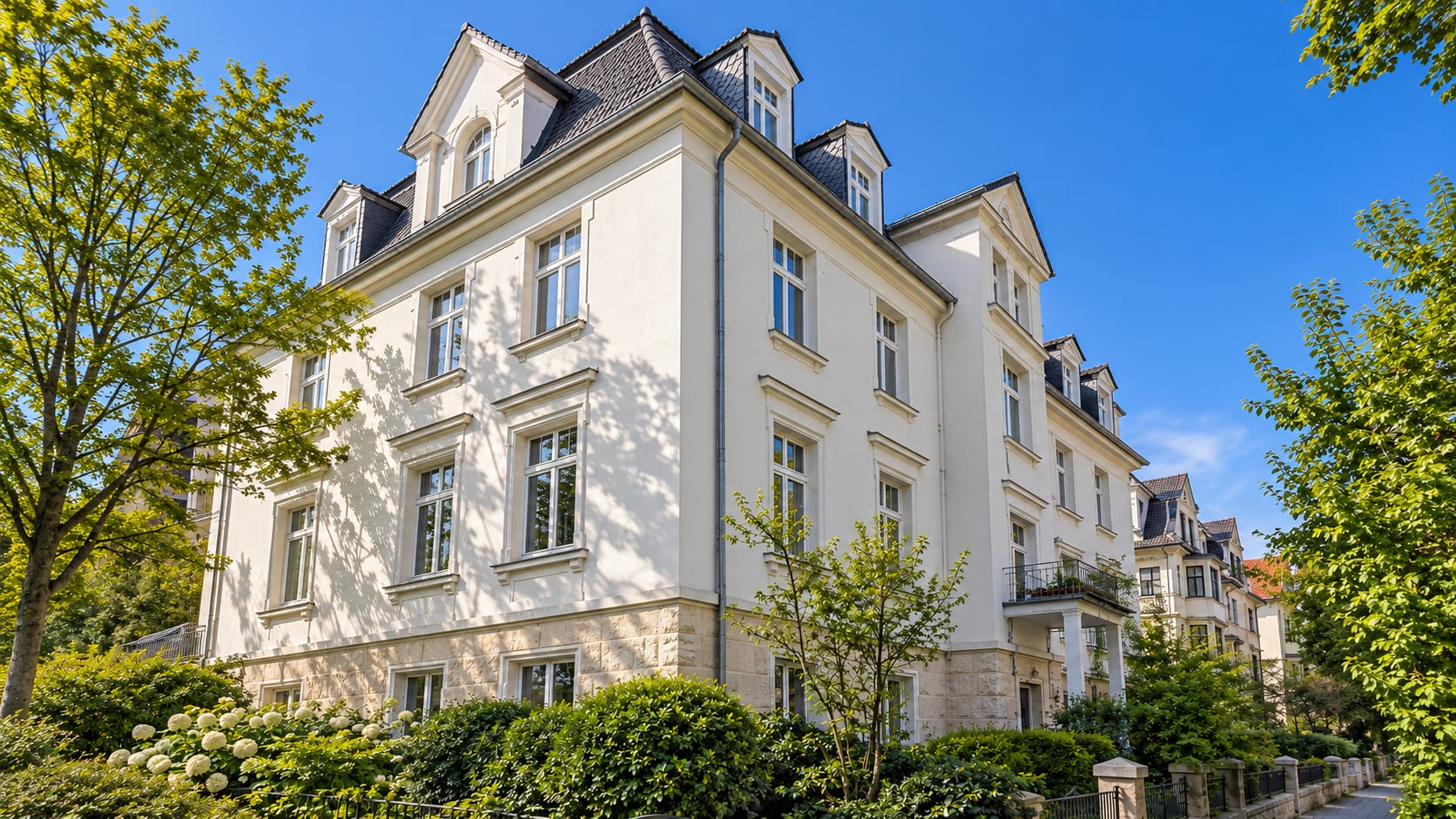 Klassisches Gründerzeit-Mehrfamilienhaus mit Mansarddach an einer baumbestandenen Straße